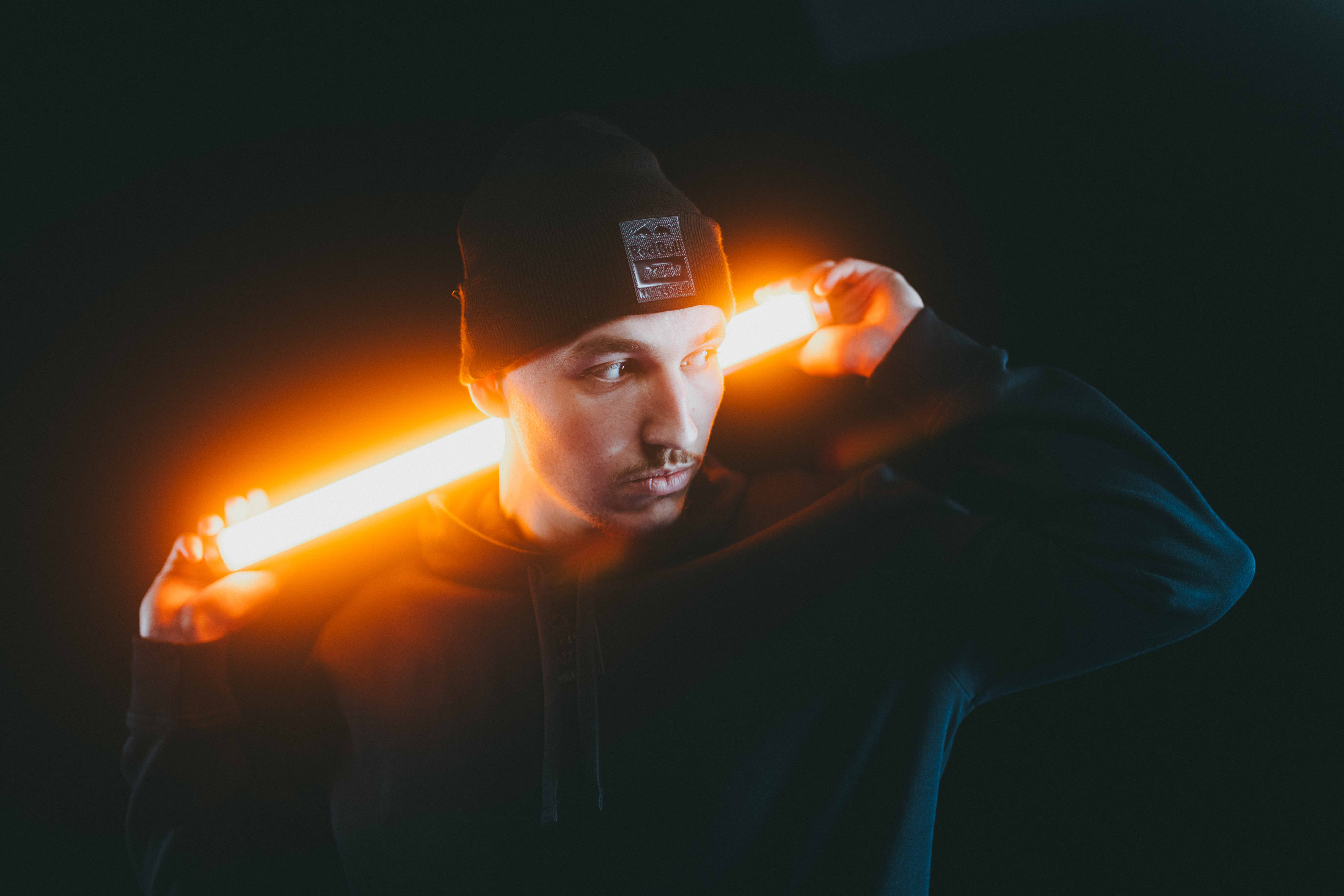 Moody portrait of a man in a beanie lit by a glowing orange light tube