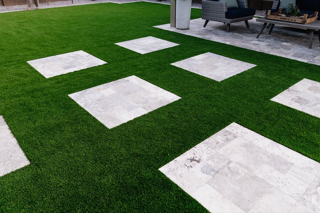 Ground-level view of large travertine stepping stones set in lush artificial turf leading to pergola