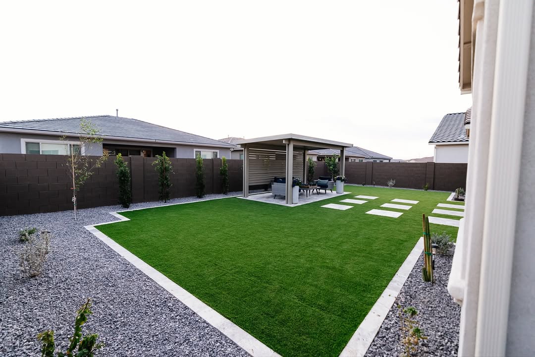 Wide aerial view of backyard with pergola, artificial turf, gravel borders, and travertine steppers