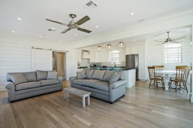 Open-plan living room with light oak hardwood, shiplap walls, and white kitchen