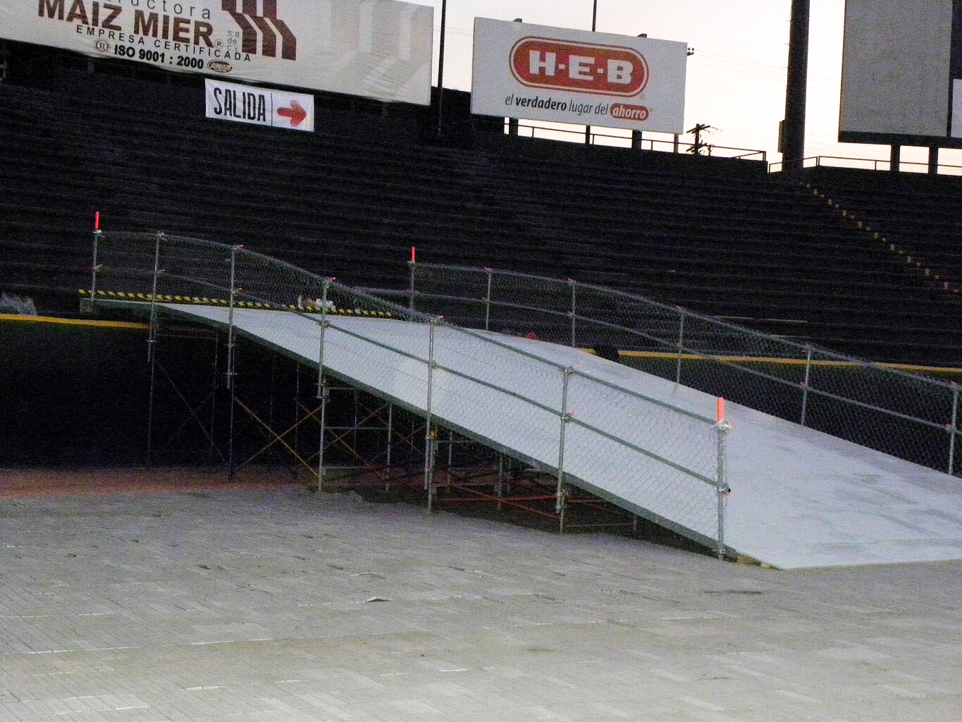 Pasarela blanca inclinada con rampa de acceso en estadio profesional, valla de seguridad amarilla y negra, estructura metálica reforzada