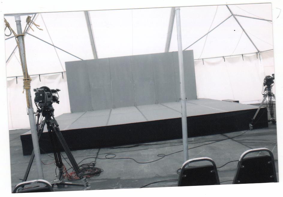 Tarima gris blanca bajo carpa transparente con estructura metálica, cámaras profesionales y equipos de video streaming