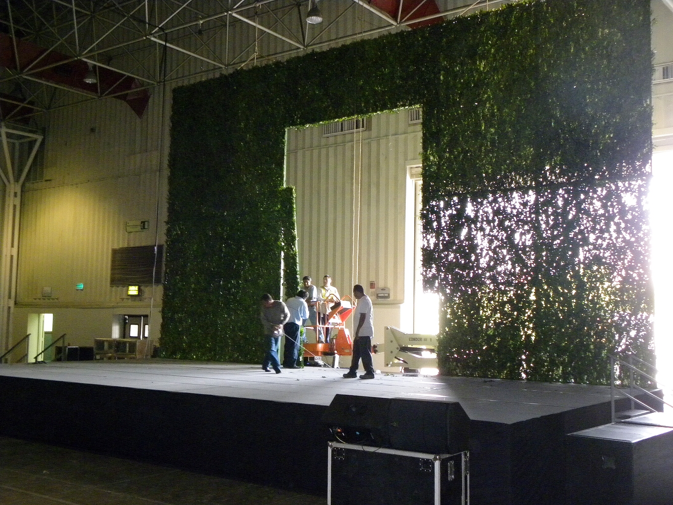 Tarima negra elevada interior con decoración de jardín vertical iluminado, escaleras de acceso y estructura industrial