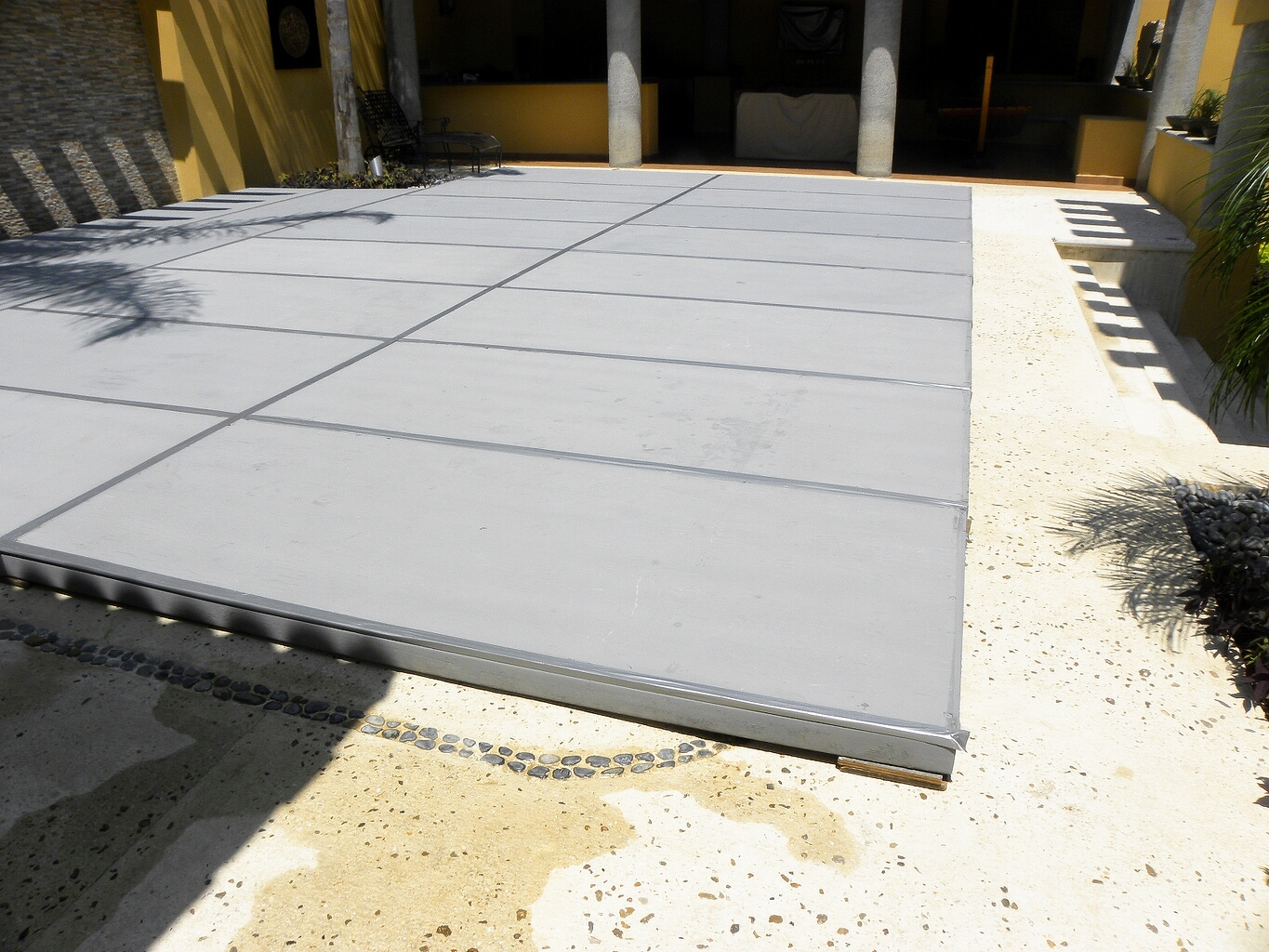 Tarima modular blanca profesional instalada en patio de cemento con columnas grises y paredes amarillas coloniales