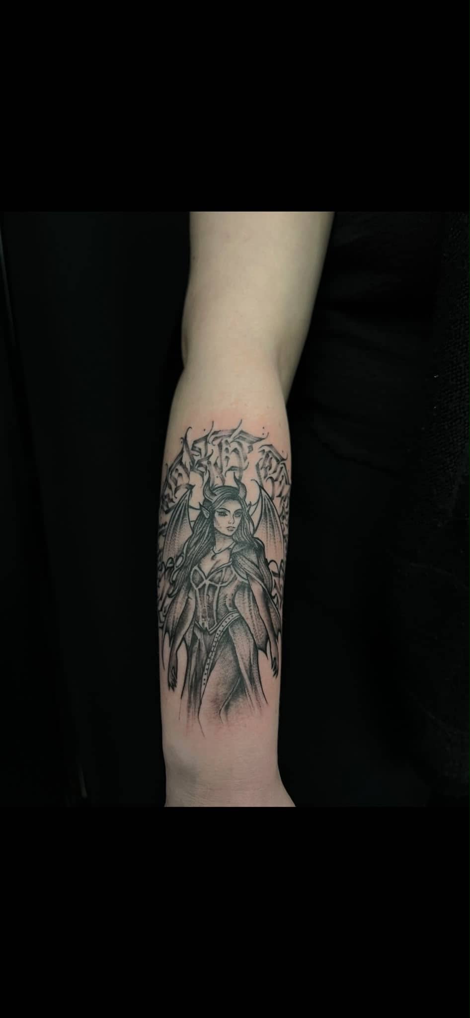 Blackwork Daemonin mit Hoernern und Fluegeln am Unterarm mit Metal-Schriftzug