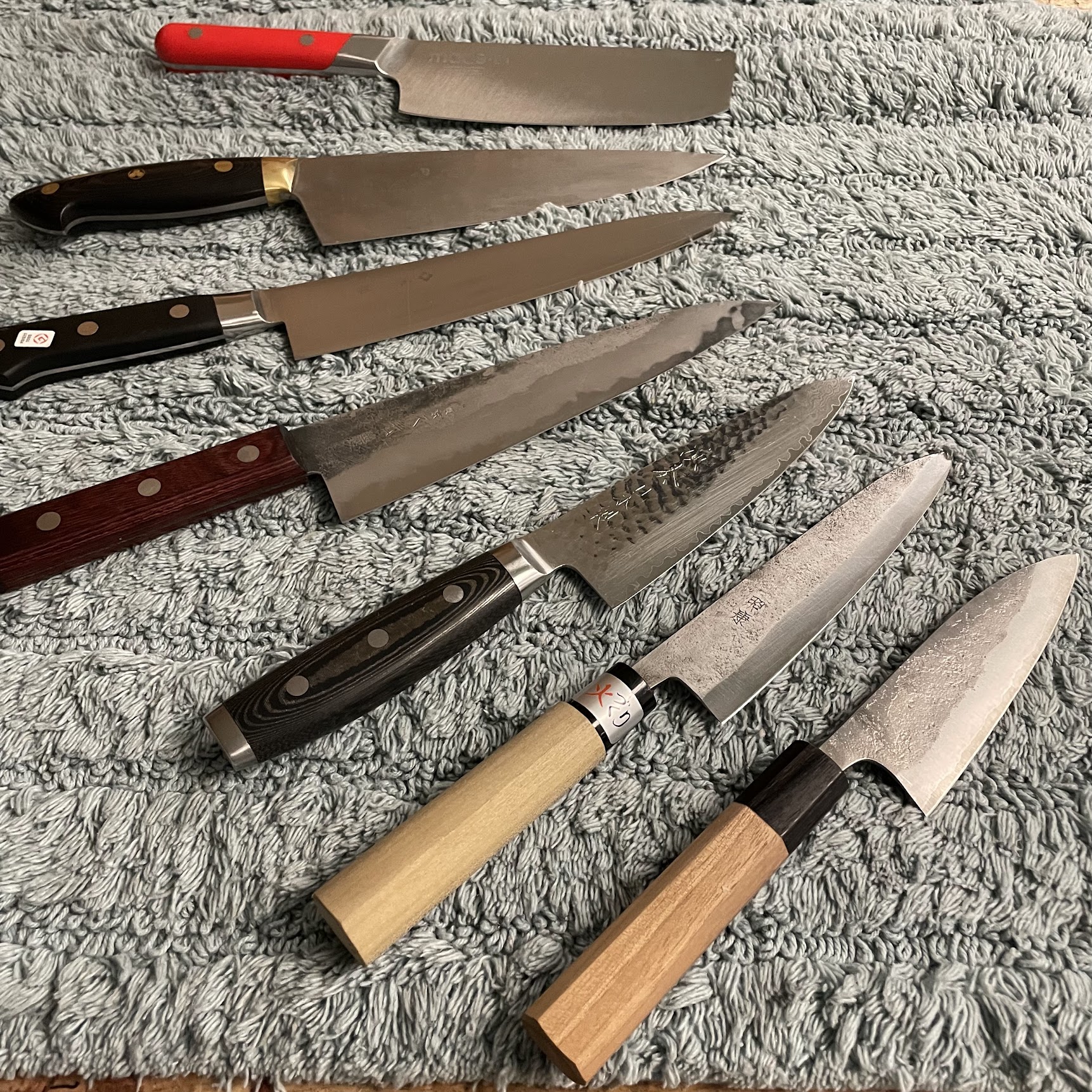 Collection of Japanese knives including yanagiba, gyuto and deba on blue towel