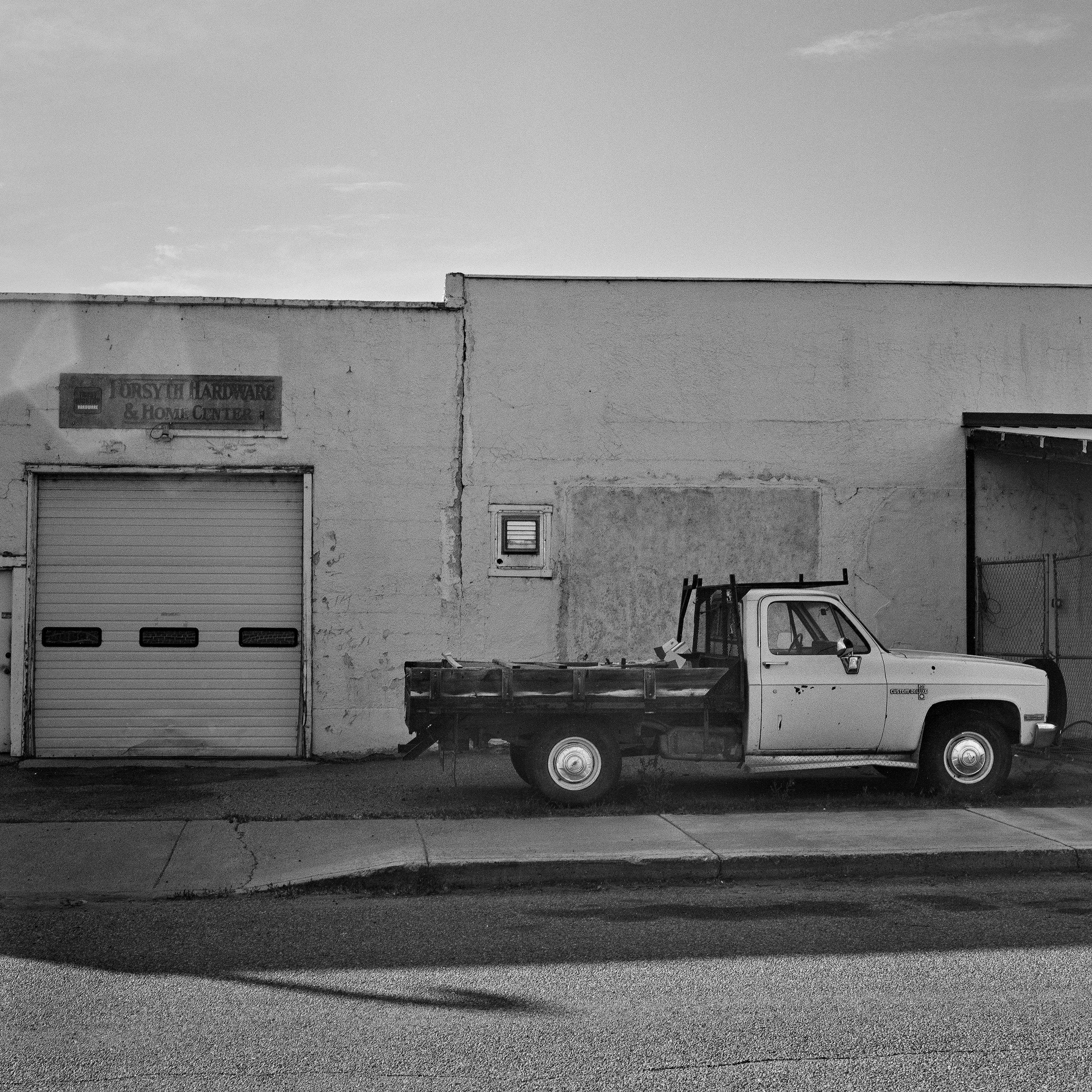 White work truck parked outside Forsyth Hardware and Home Center with weathered stucco walls