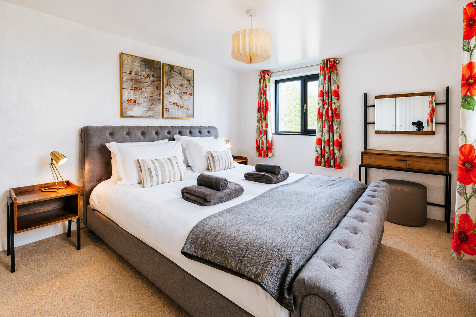 Stylish king bedroom with tufted grey headboard, poppy-print curtains, and gold bedside lamp