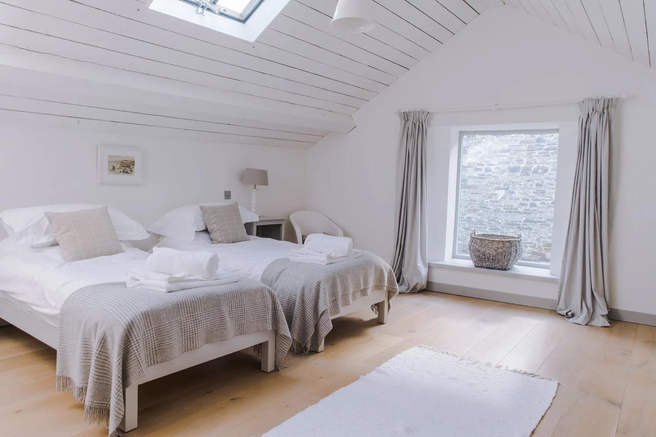 Lofted twin bedroom with white-washed vaulted ceiling, skylight, and oak floor