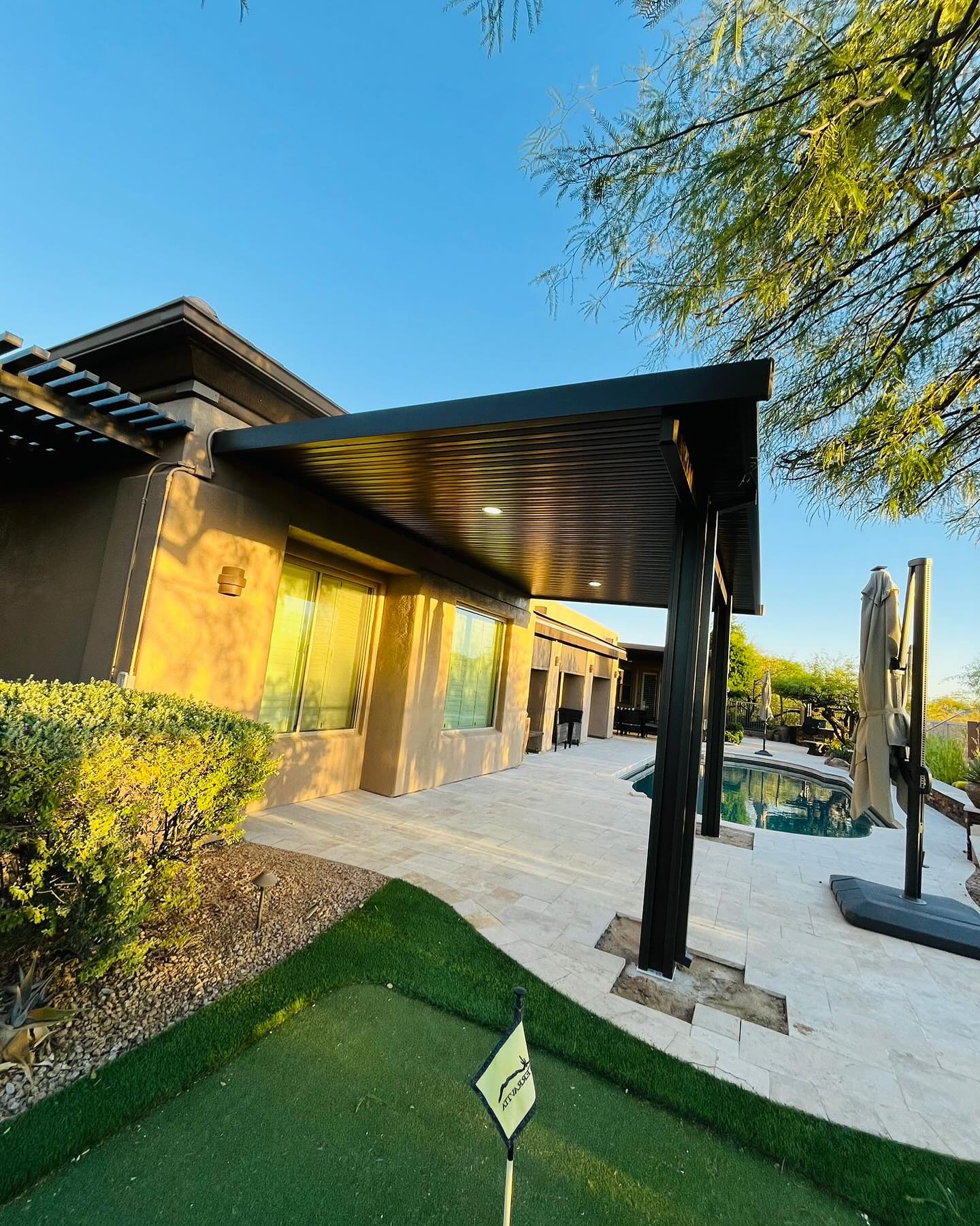 Louvered pergola over a paver patio beside a backyard pool
