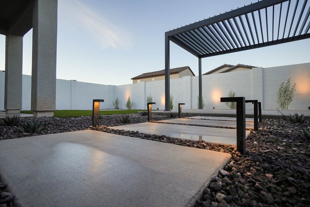 Dusk view of white pergola with louvered wall and paver walkway