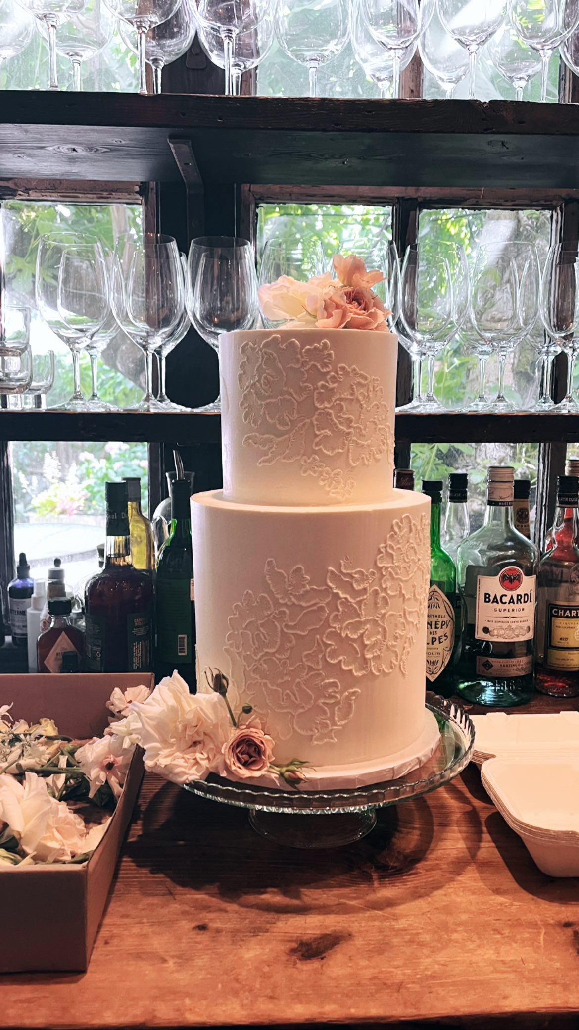 White two-tier wedding cake with embossed floral pattern and blush roses at bar