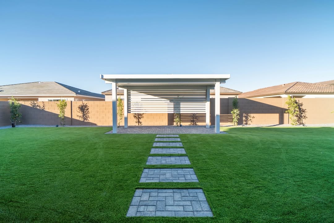 White louvered patio cover with paver walkway across green turf