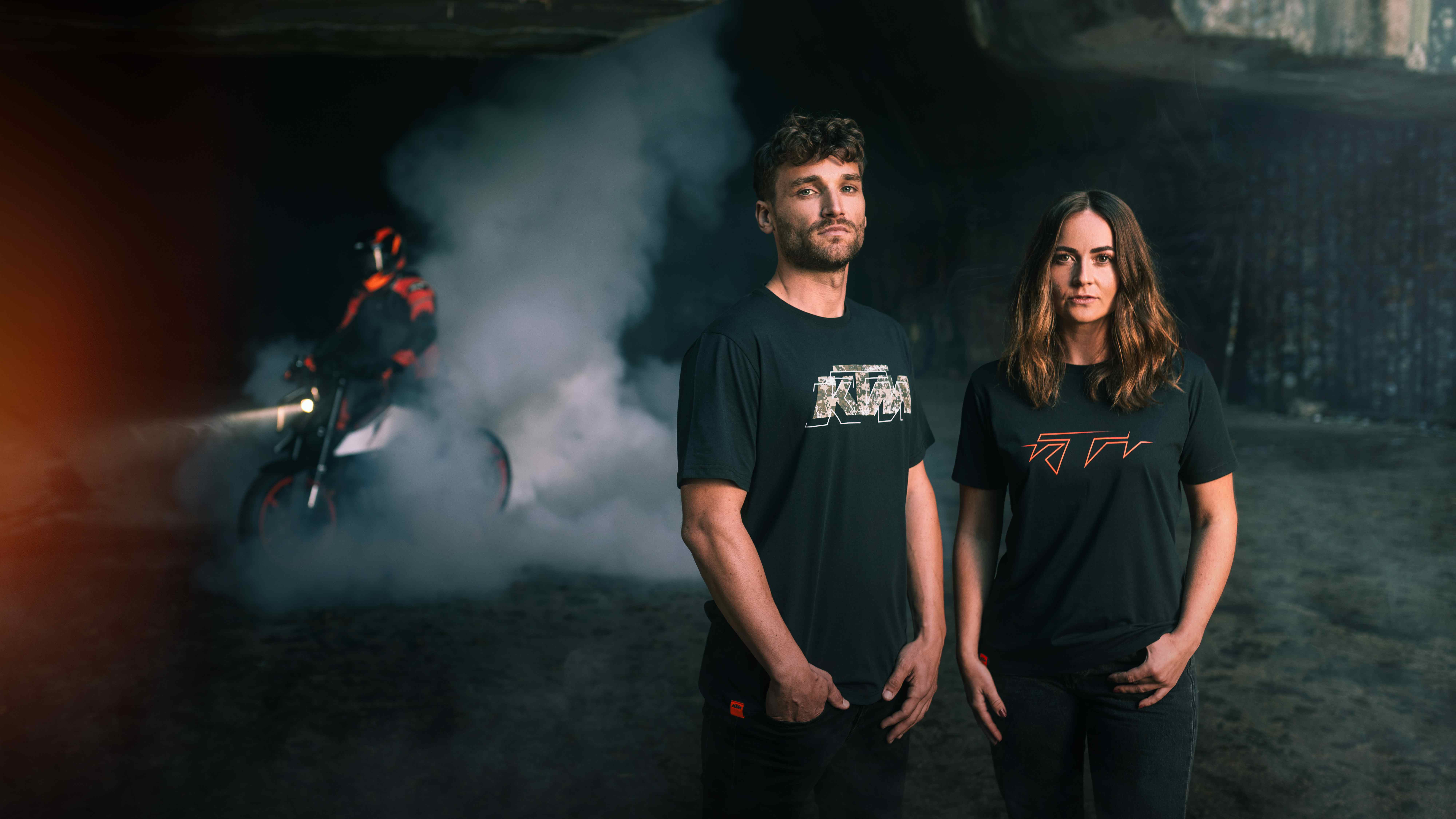 Man and woman in black KTM t-shirts with a smoky burnout in the background