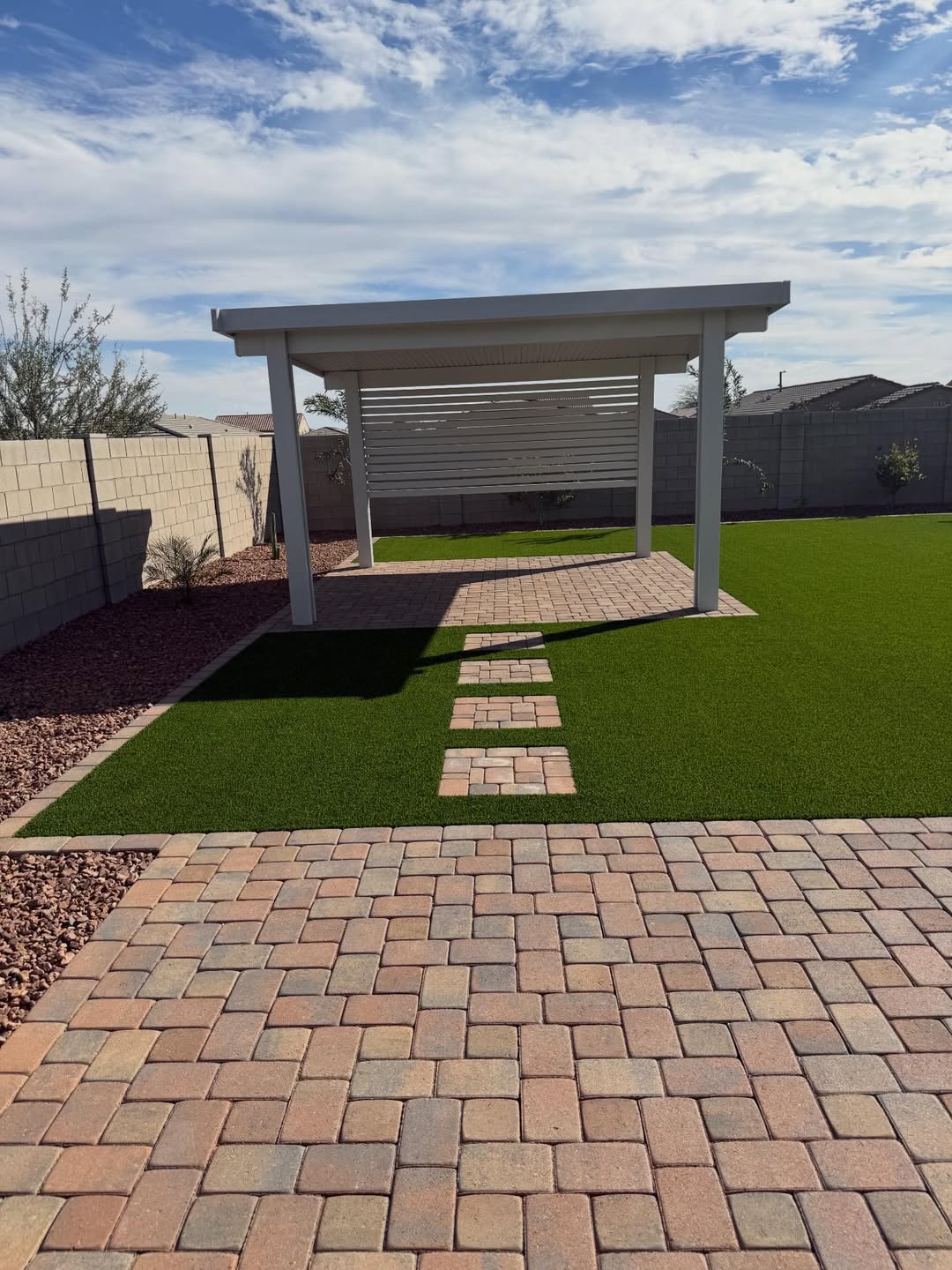 White attached patio cover with paver stepping-stone path through turf