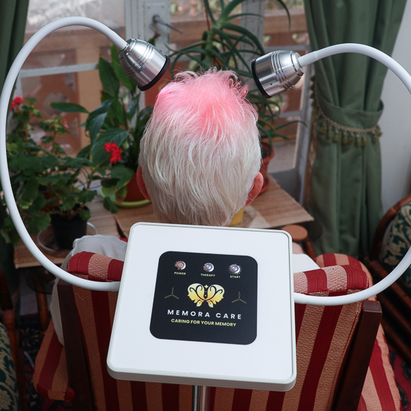 Seated person viewed from behind with both MemoraCare light heads positioned around their head and the control unit visible in front