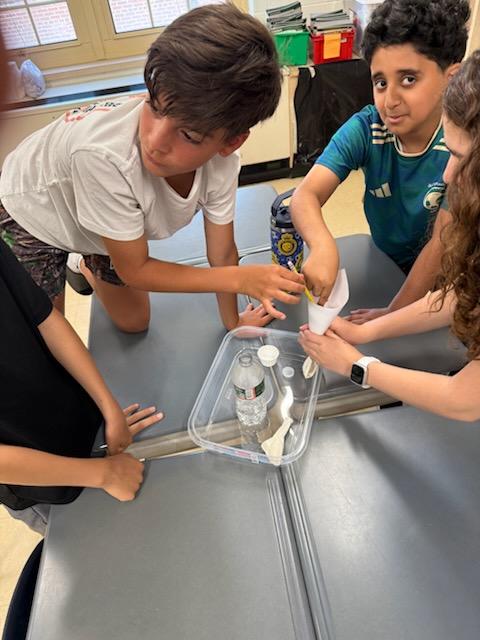 Students conducting a hands-on experiment with a paper cone and bottles at a classroom table