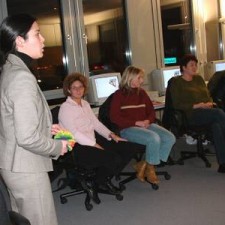 Frau präsentiert vor vier sitzenden Erwachsenen im Computerraum