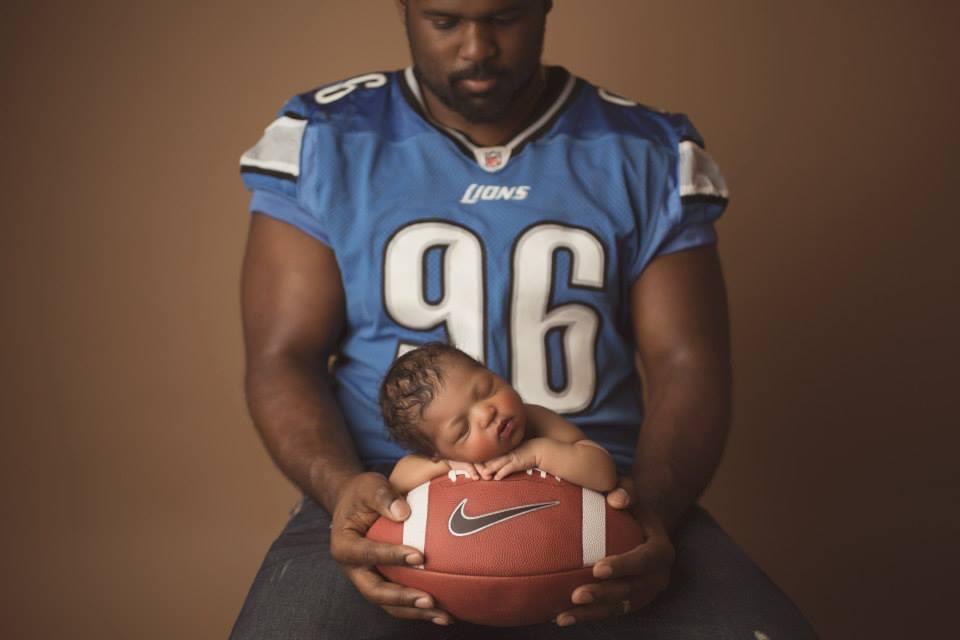 Andre Fluellen in Detroit Lions jersey holding newborn daughter on a football