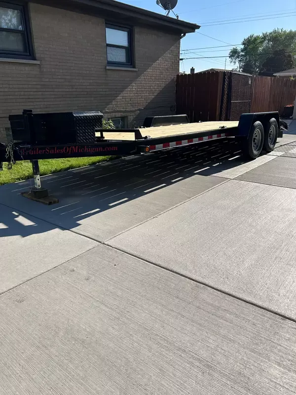 Full side view of DTC Rentals 7x20 flatbed car hauler trailer on concrete driveway