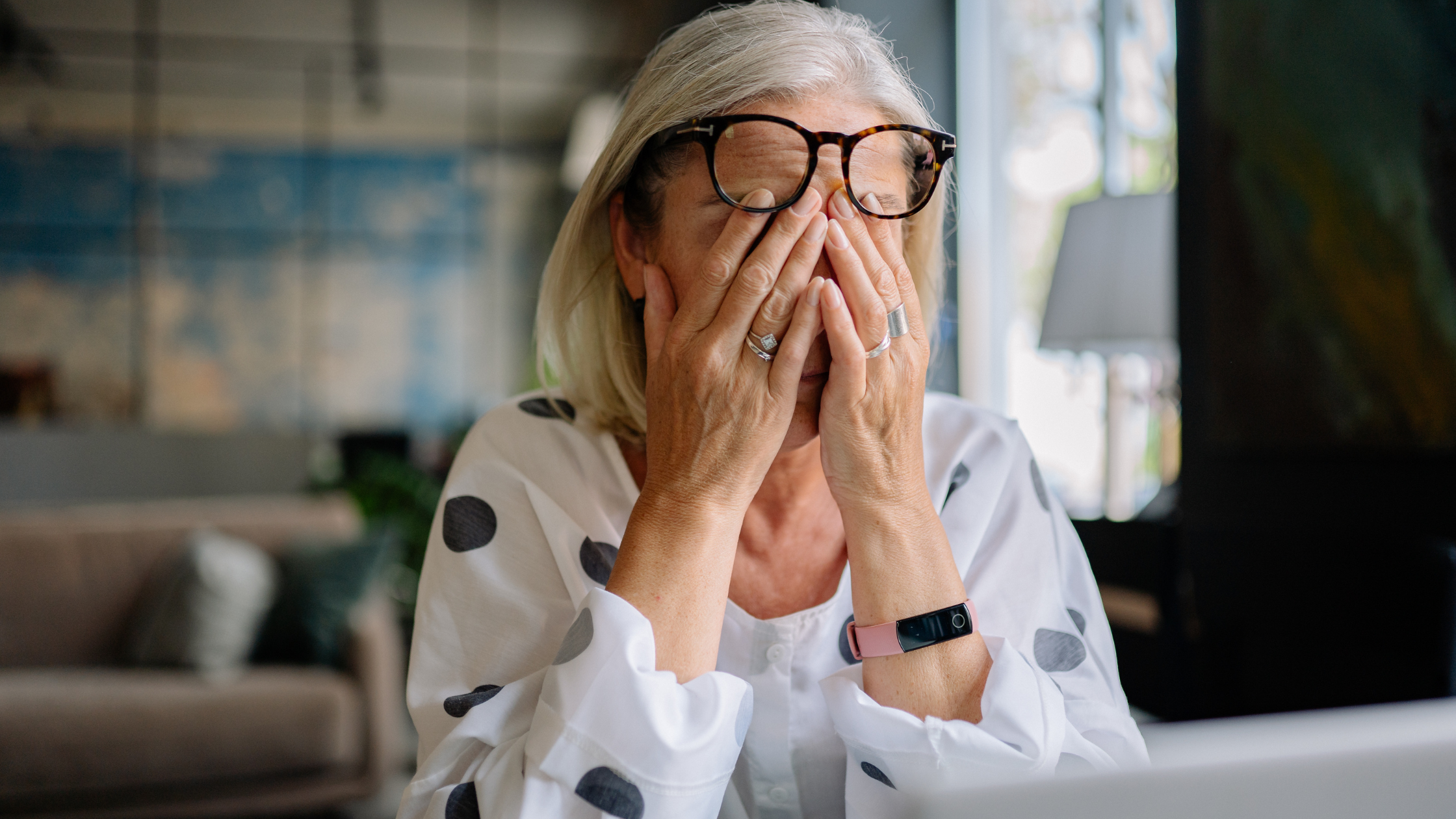 Stressed woman with glasses rubbing her eyes while sitting at her laptop