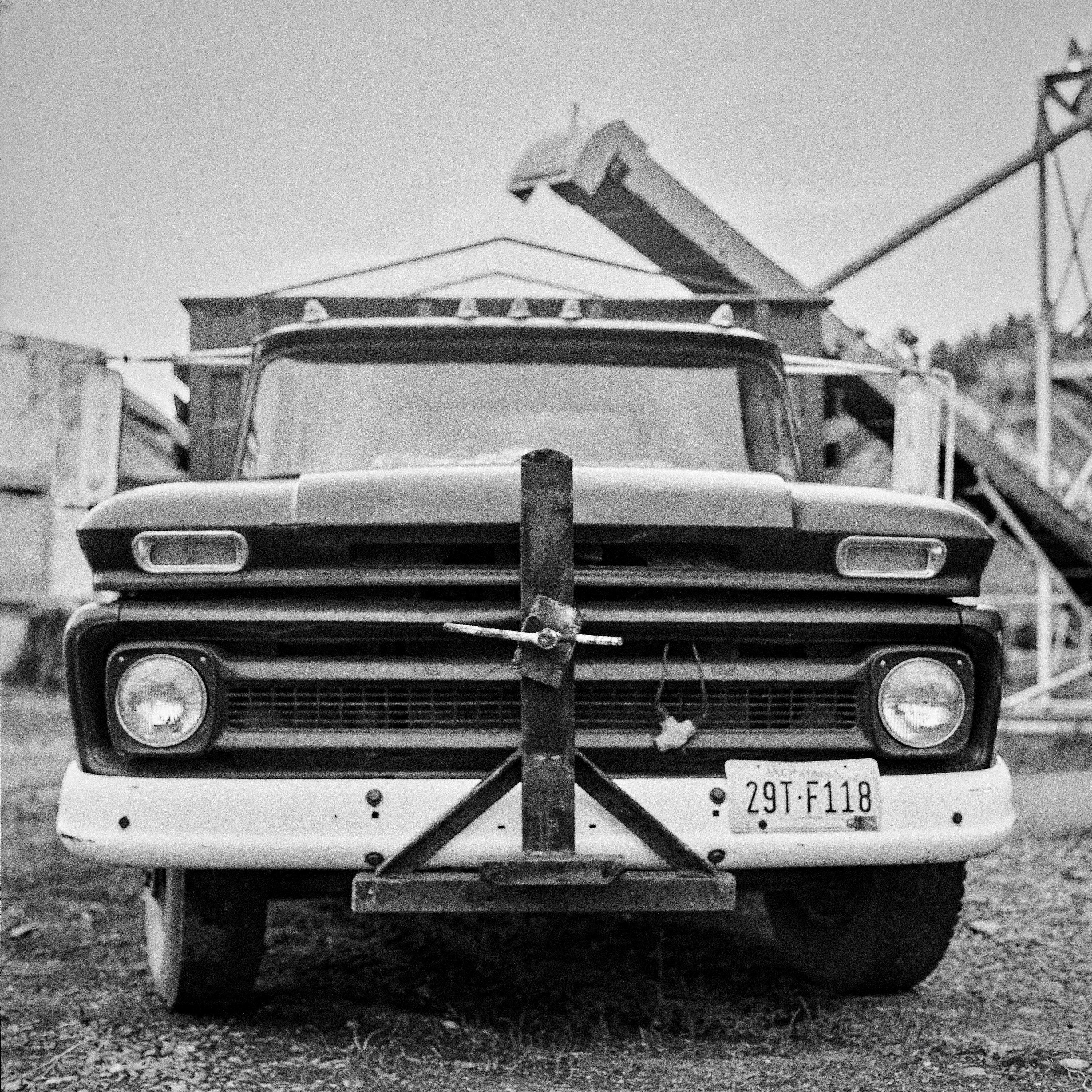 Front view of vintage Chevrolet truck with Montana license plate and grain elevator behind