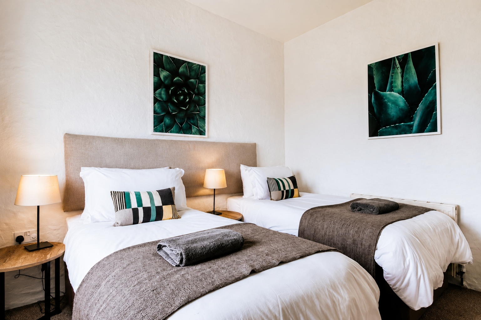 Twin bedroom with linen headboard, warm lamps, geometric cushions, and large botanical prints