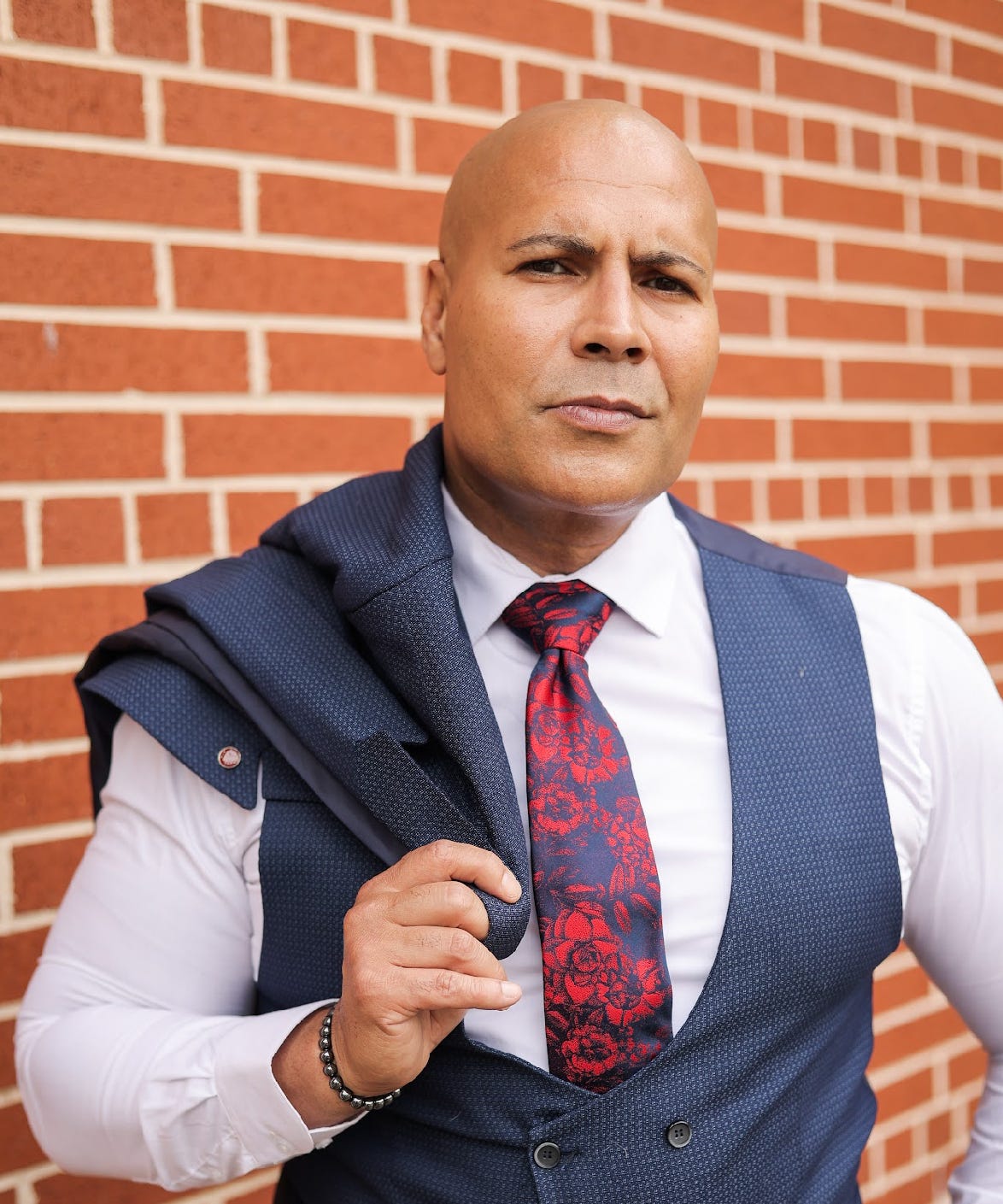 Maven Huffman in a tailored vest and tie against a brick wall