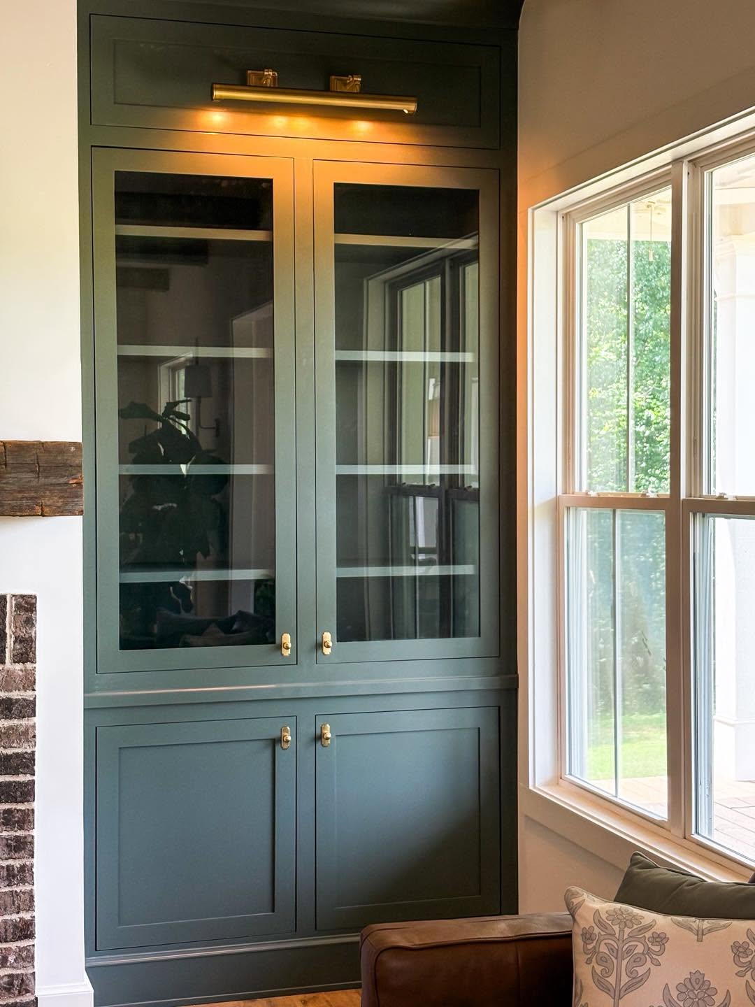 Custom built-in display cabinet finished in deep green with brass hardware and picture light