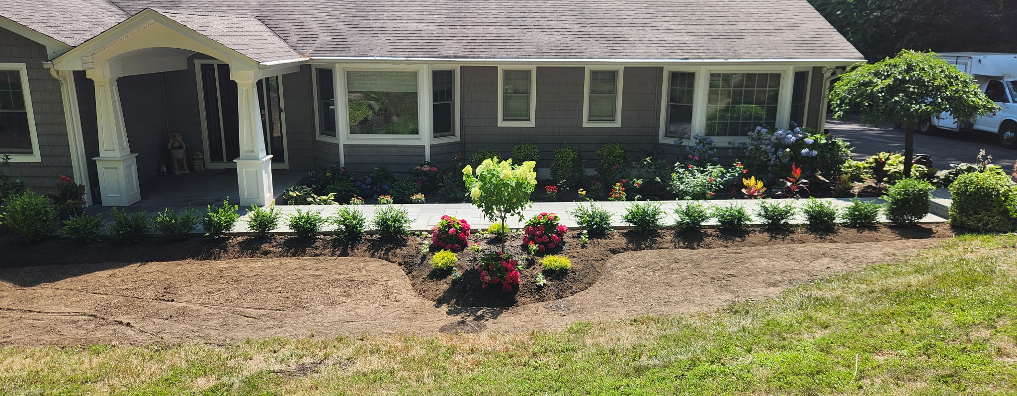 Front yard garden design with new shrubs and colorful flowers along a walkway