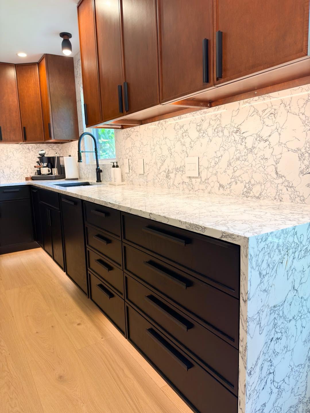 Kitchen remodel with cherry and black cabinetry and a waterfall marble island