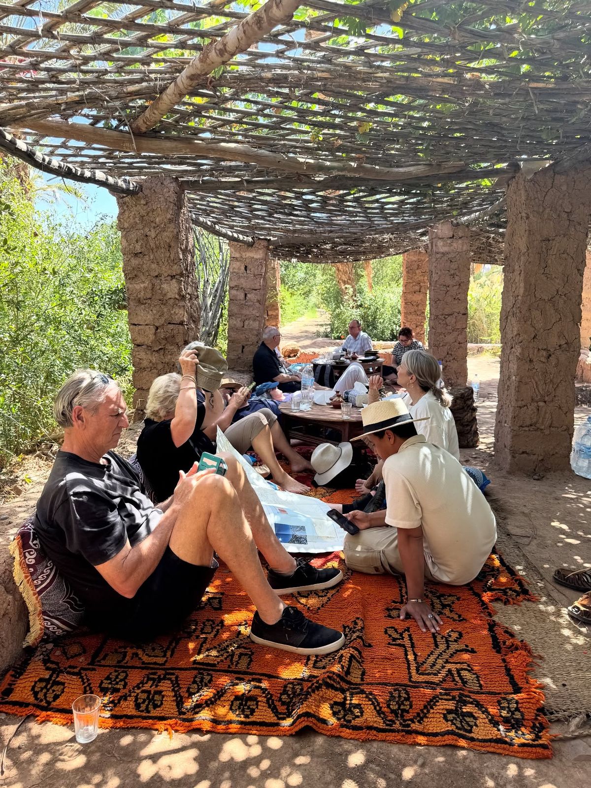 Tourists gathered under wooden pergola in traditional Moroccan garden on colorful rugs