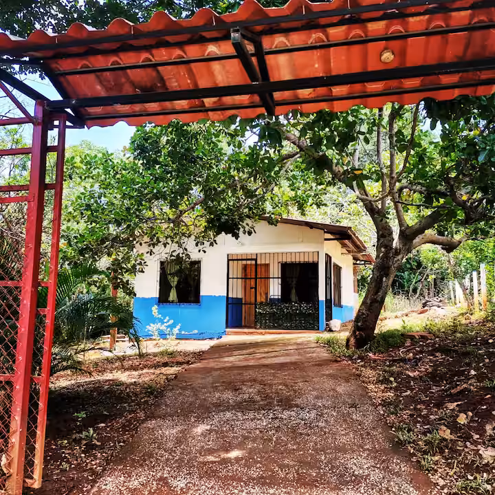 Fachada blanca y azul de la casita bajo un techo rojo, rodeada de árboles