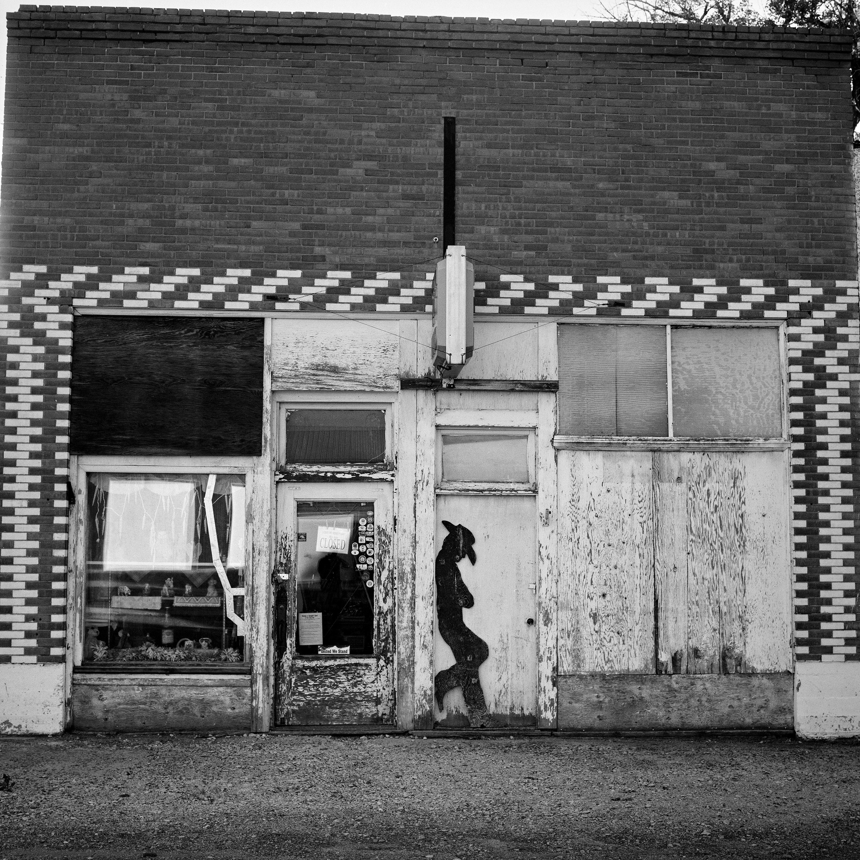 Abandoned storefront with checkered brick pattern and cowboy silhouette cutout on weathered facade