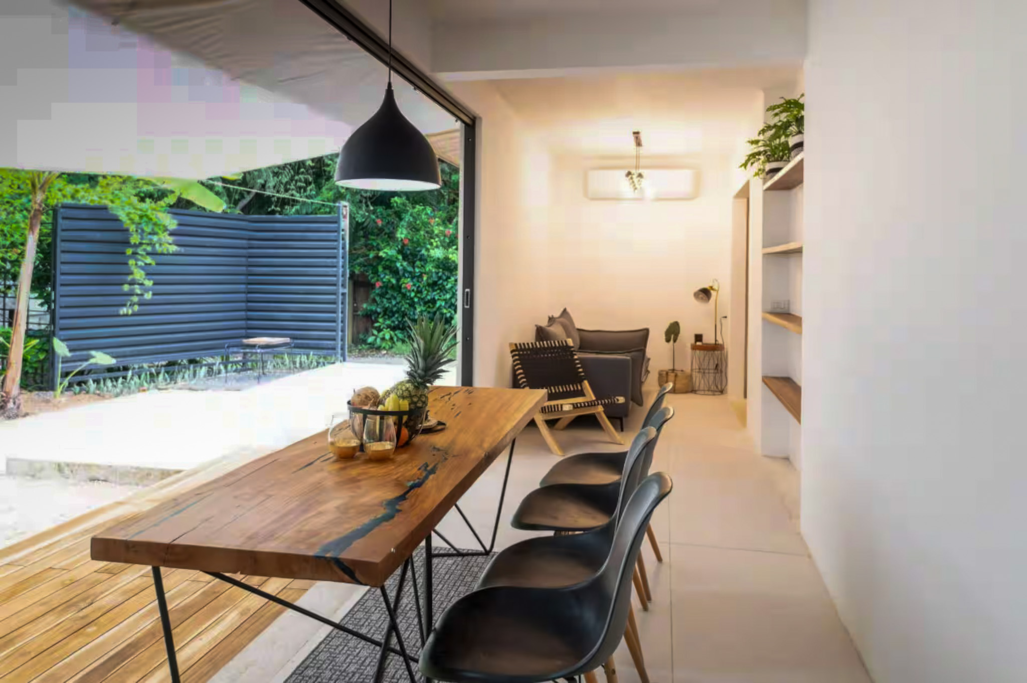 Dining and living area with tropical garden views, live-edge table, and black pendant lamp