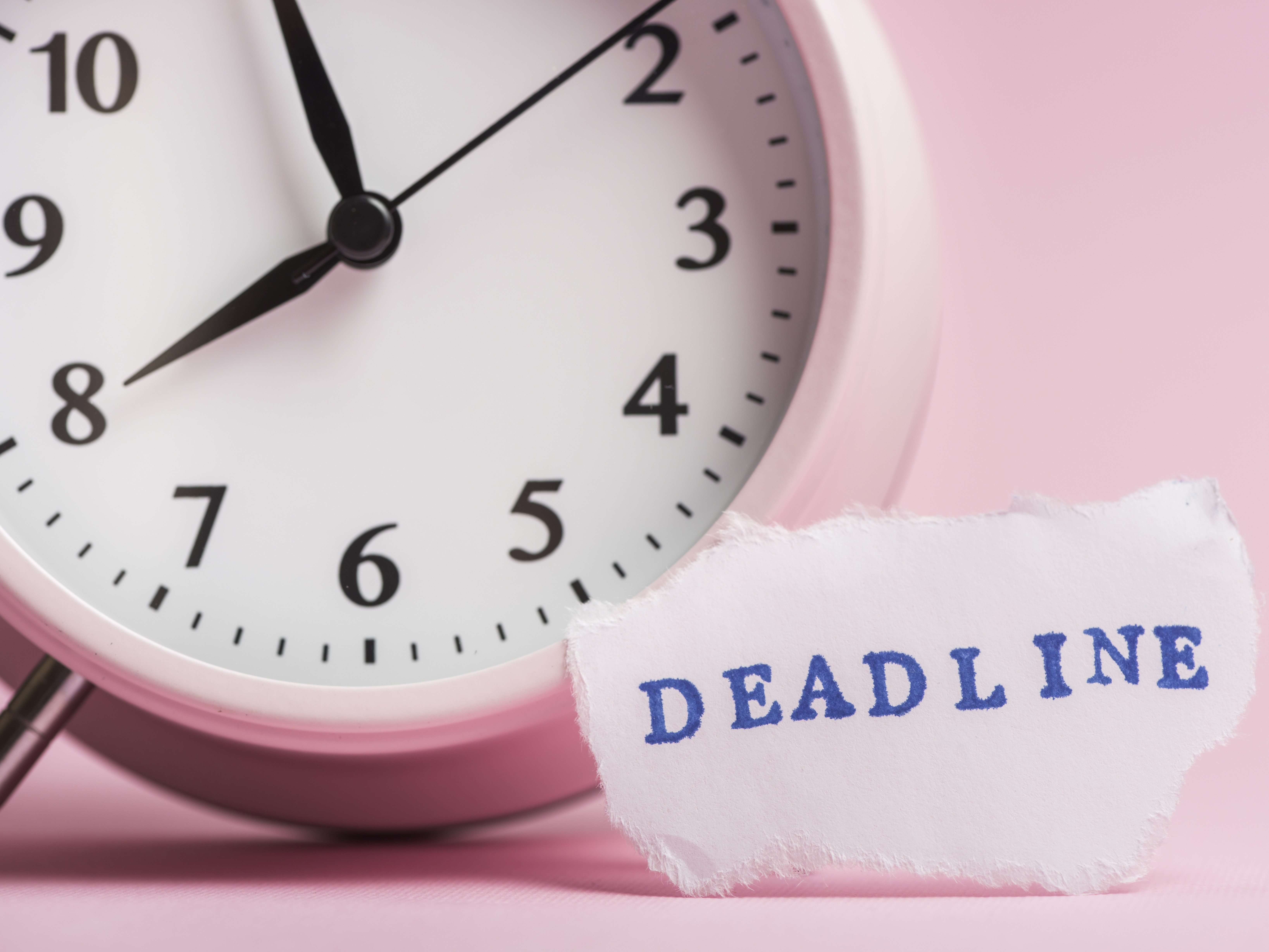 Pink alarm clock beside a torn note reading DEADLINE