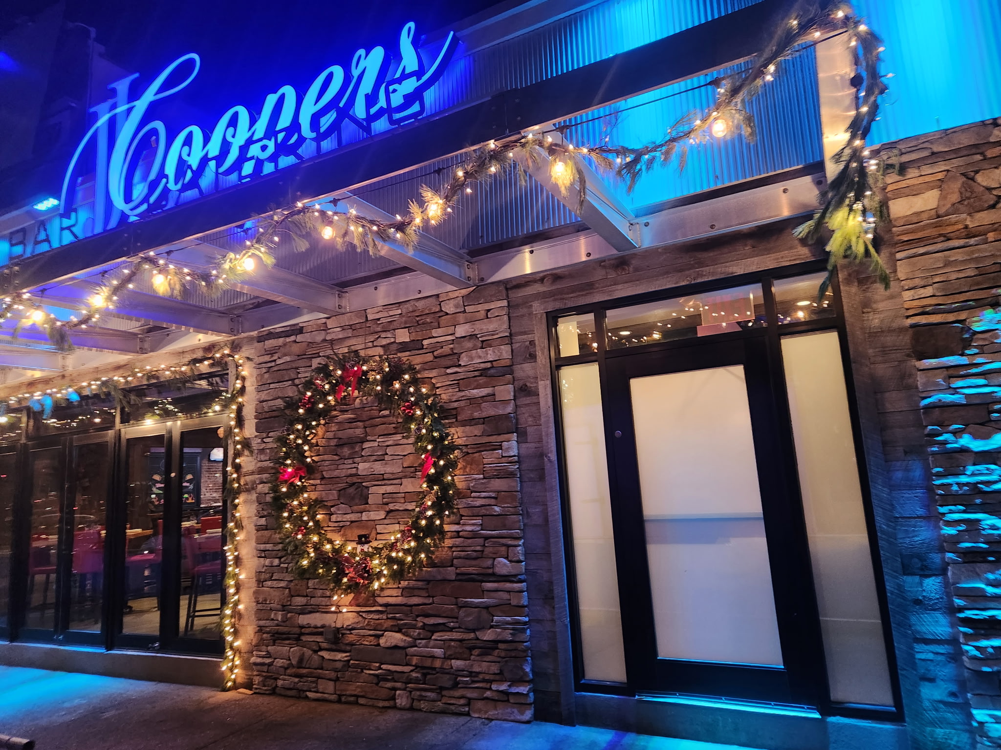 Storefront decorated with Christmas lights, garlands, and a large wreath on a stone facade