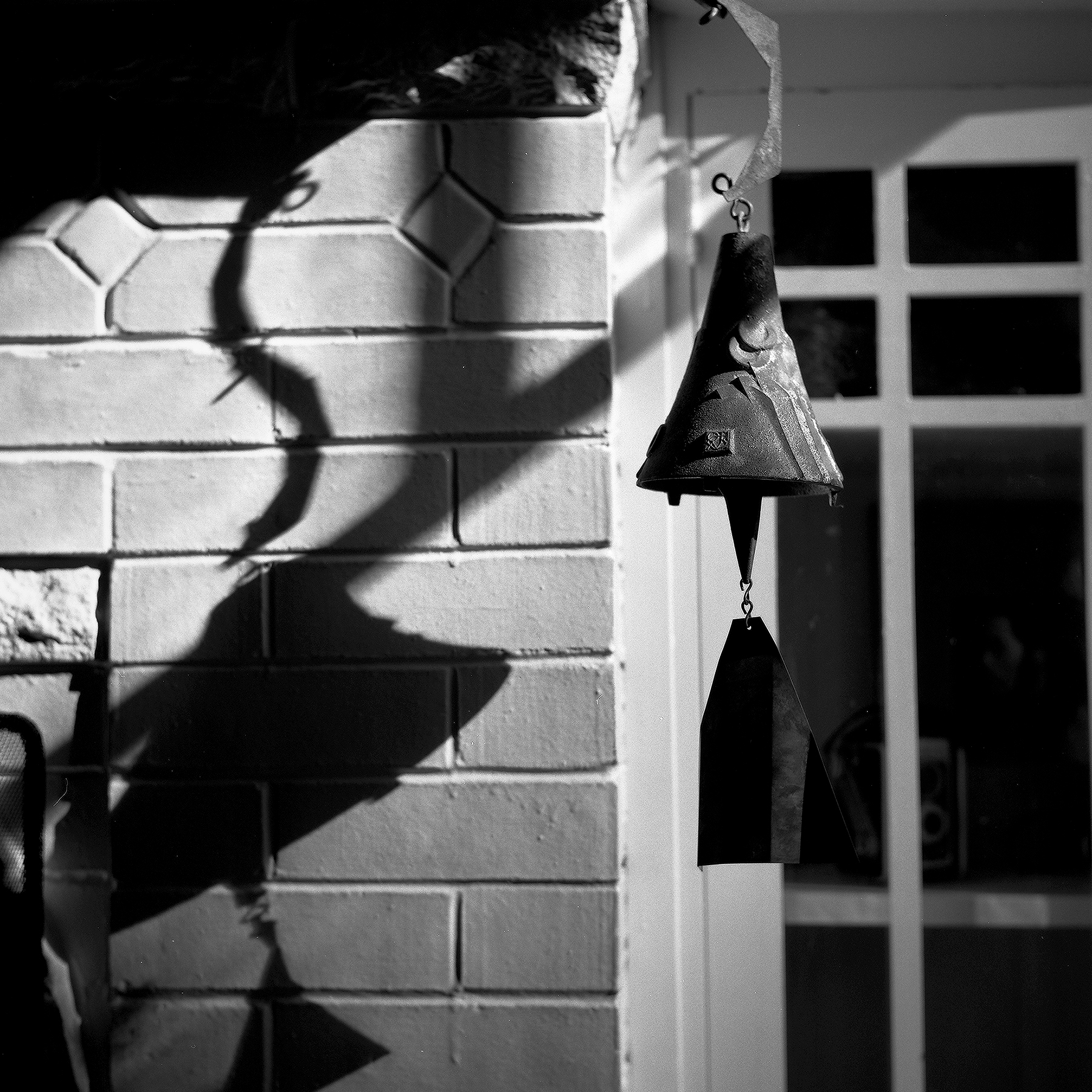 Japanese-style iron wind chime bell hanging against white brick wall with branch shadows creating delicate patterns