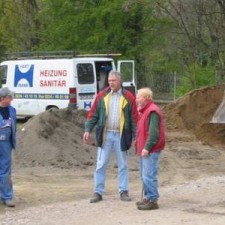 Drei Männer auf dem Baugelände, Heizung/Sanitär-Transporter im Hintergrund