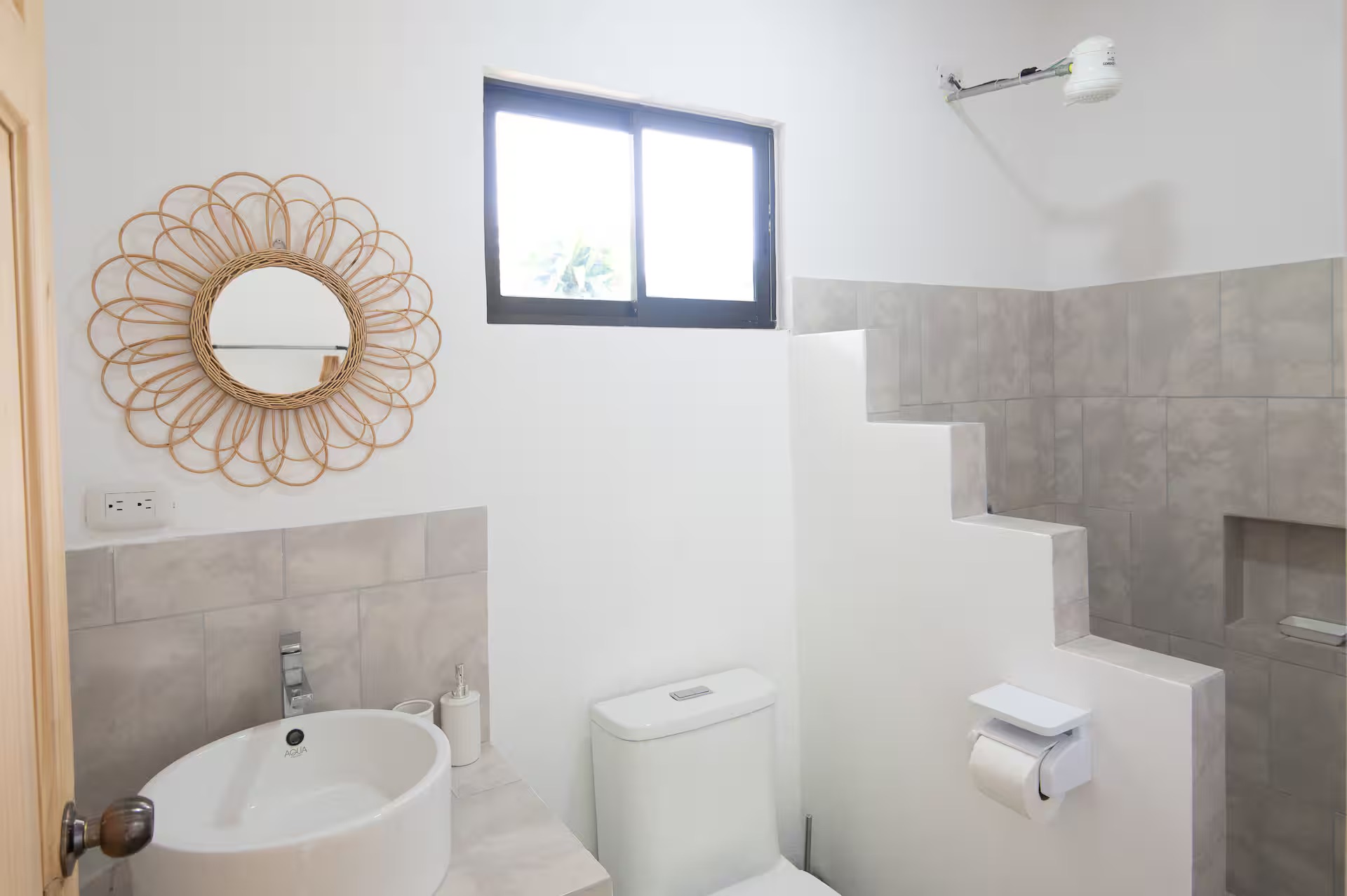 Bathroom with rattan sunflower mirror, grey tile, open shower, toilet and window