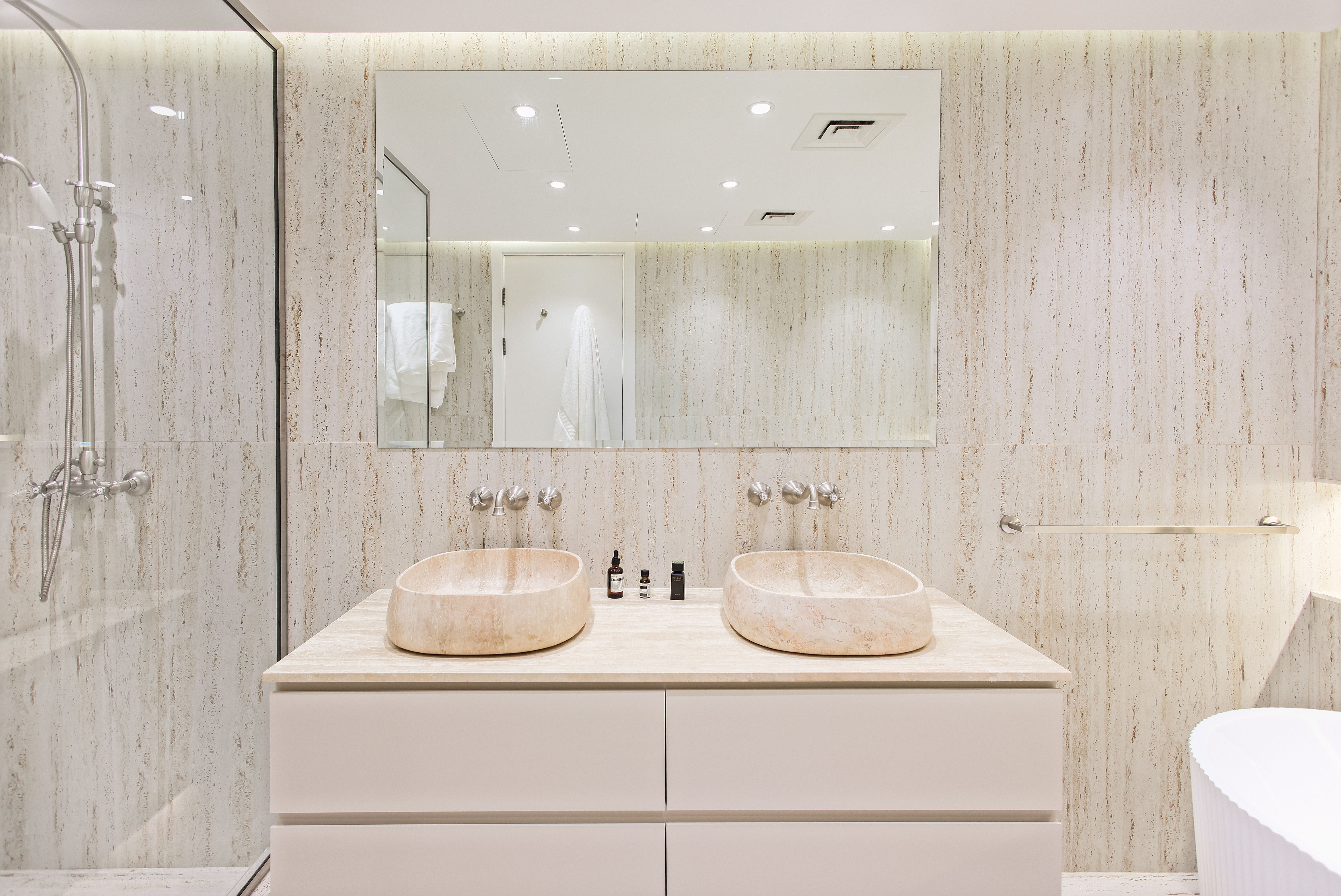 Bathroom with travertine walls and dual stone vessel sinks