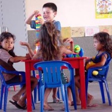 Vier Kinder am Tisch, Junge zeigt ein Spielzeug