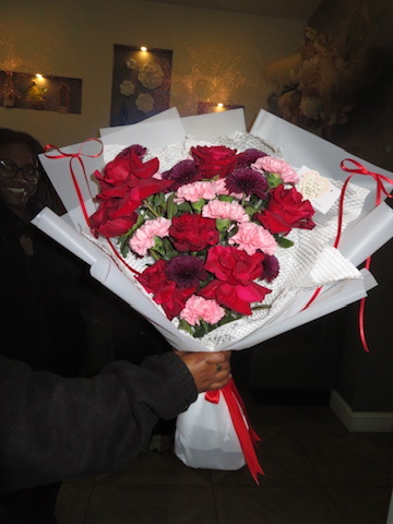 Red roses, burgundy flowers and pink carnations bouquet in white paper with red ribbons