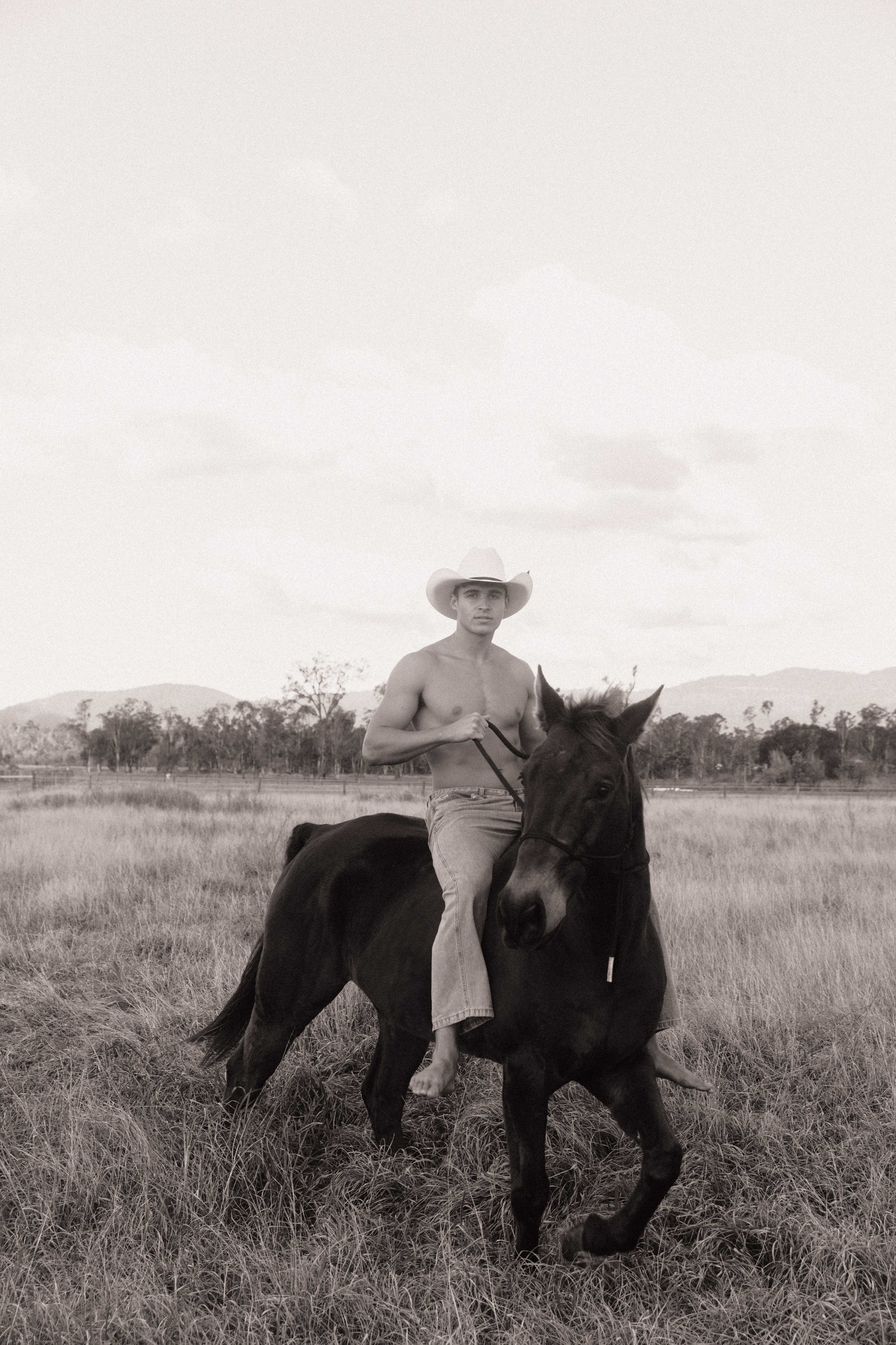Cowboy riding bareback on dark horse in open field sepia tone