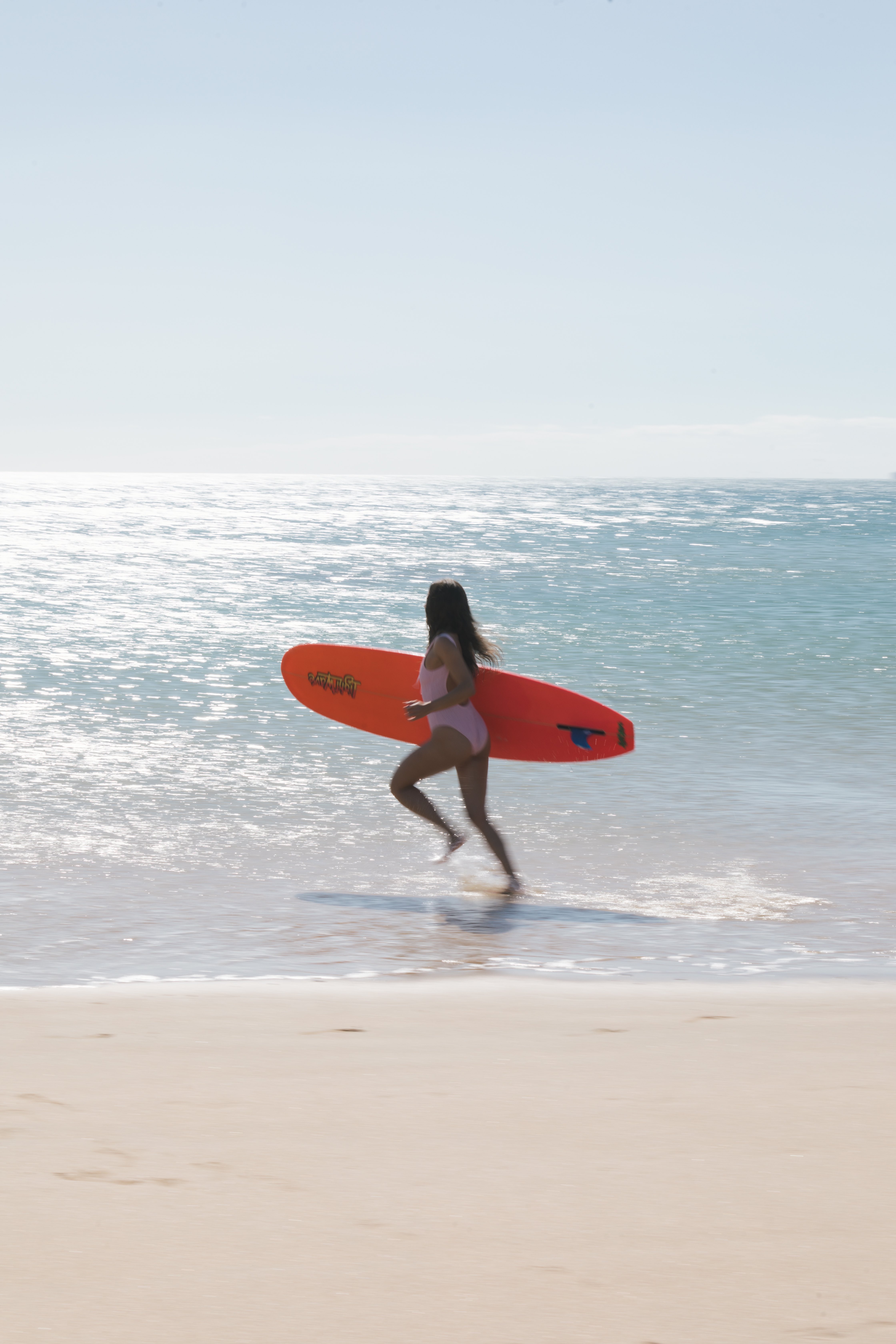 Model running into ocean with orange surfboard motion blur