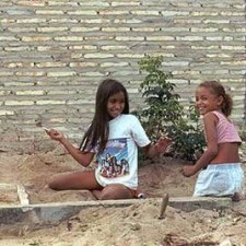 Zwei Mädchen spielen im Sand vor einer Backsteinmauer