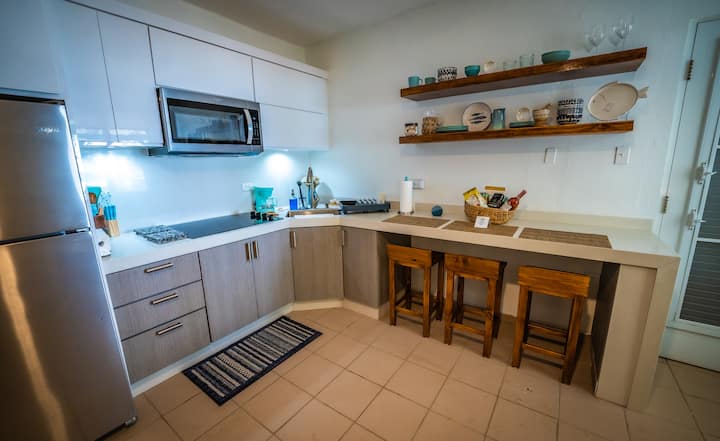 Fully equipped kitchen with stainless steel appliances, gas stove, open shelves with dishware, and breakfast bar