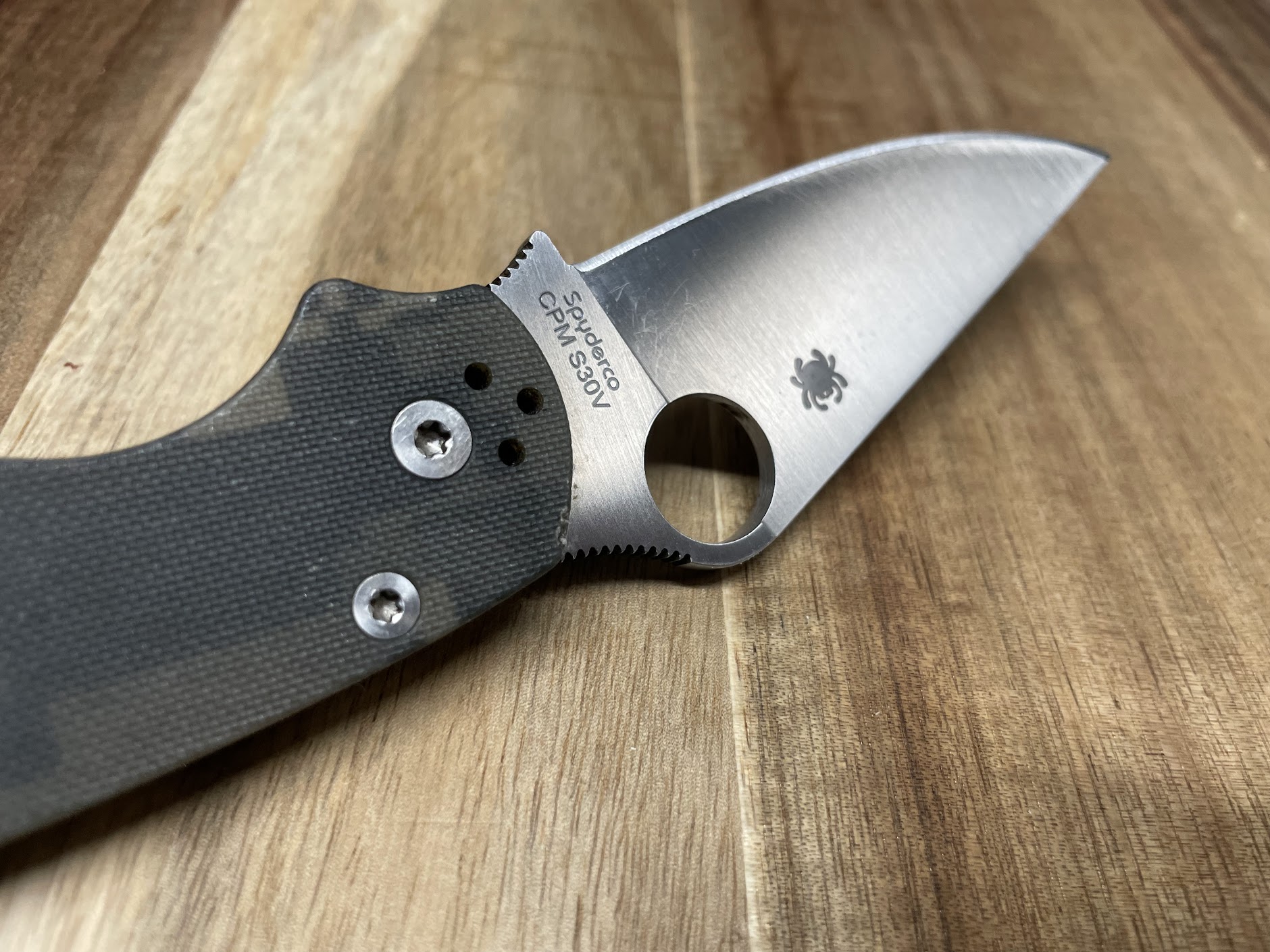 Close-up of a Spyderco CPM S30V folding knife with black G-10 handle on a wooden surface