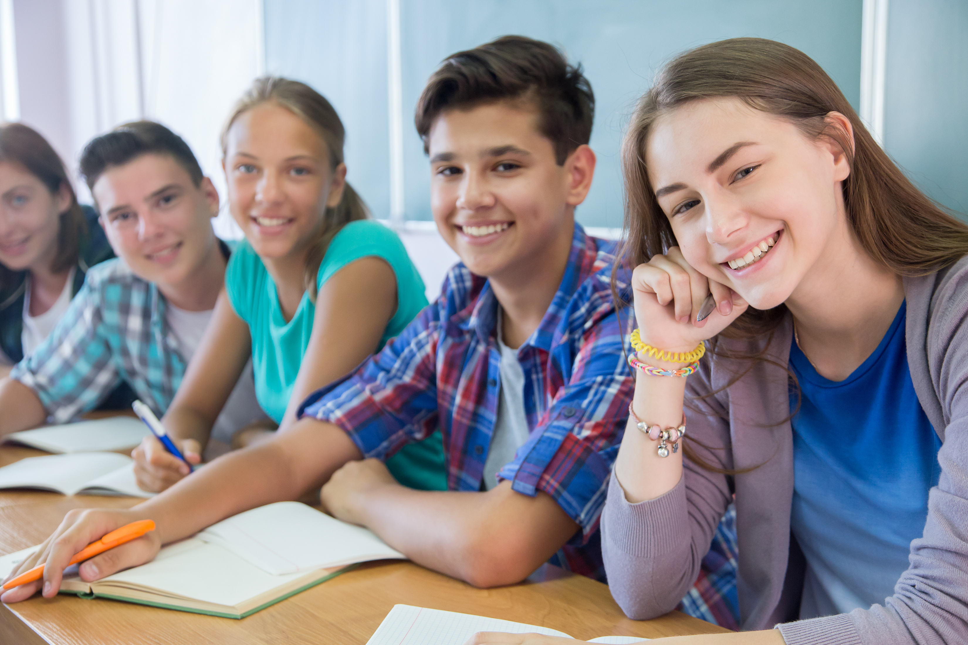 Smiling students sitting together at classroom desks with notebooks, engaged in learning