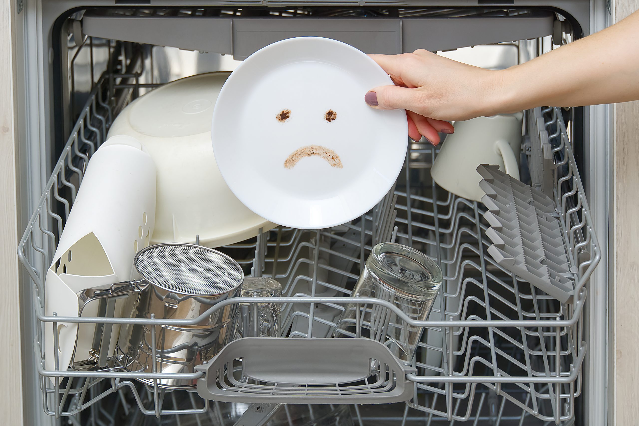 Dishwasher with poorly cleaned dishes showing a sad face on a plate